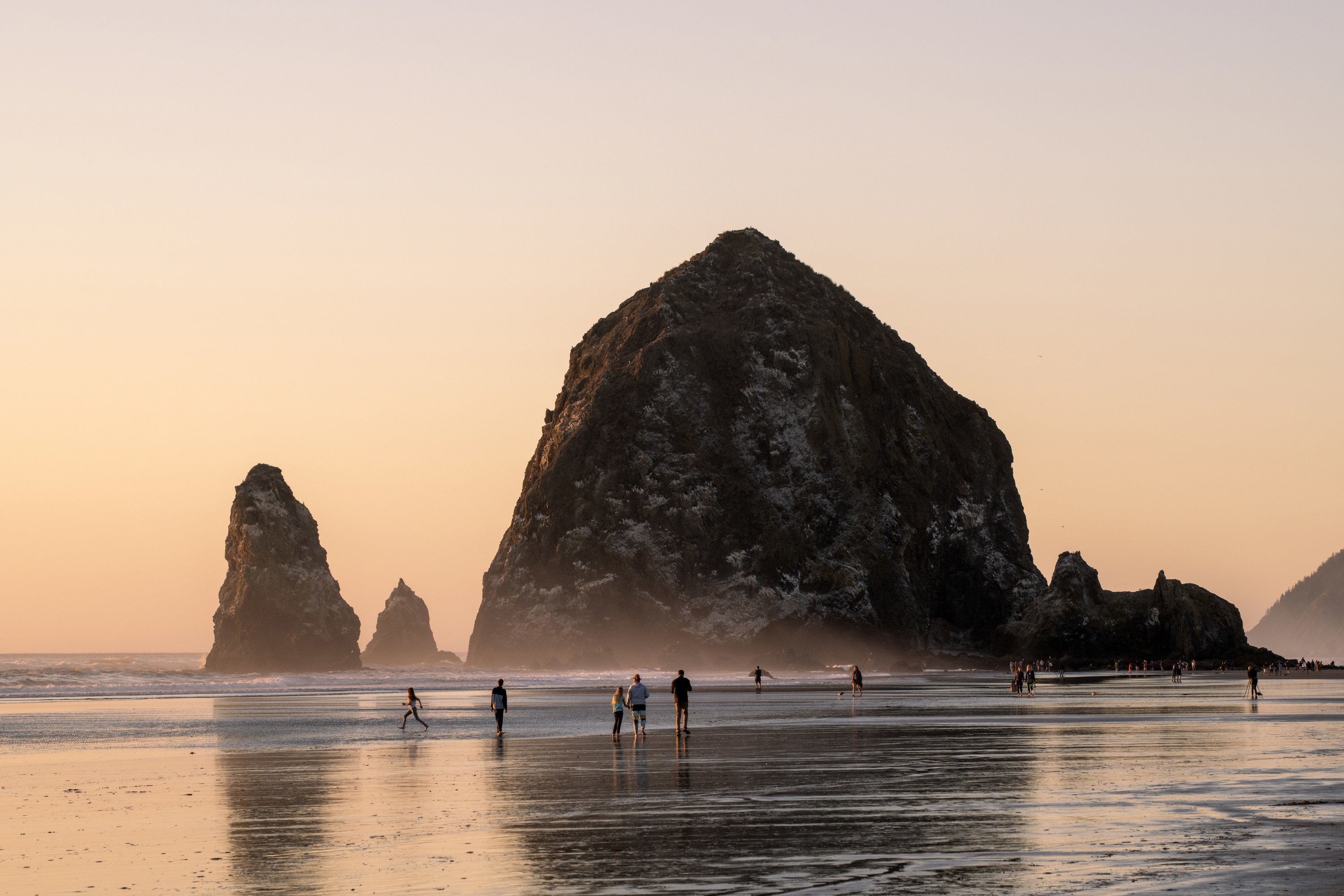 People walk by the enormous rocks at Cannon Beach in Oregon during a misty sunset