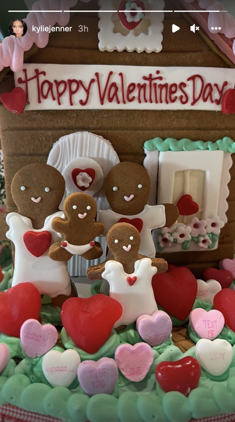 A gingerbread house with four gingerbread people standing in front