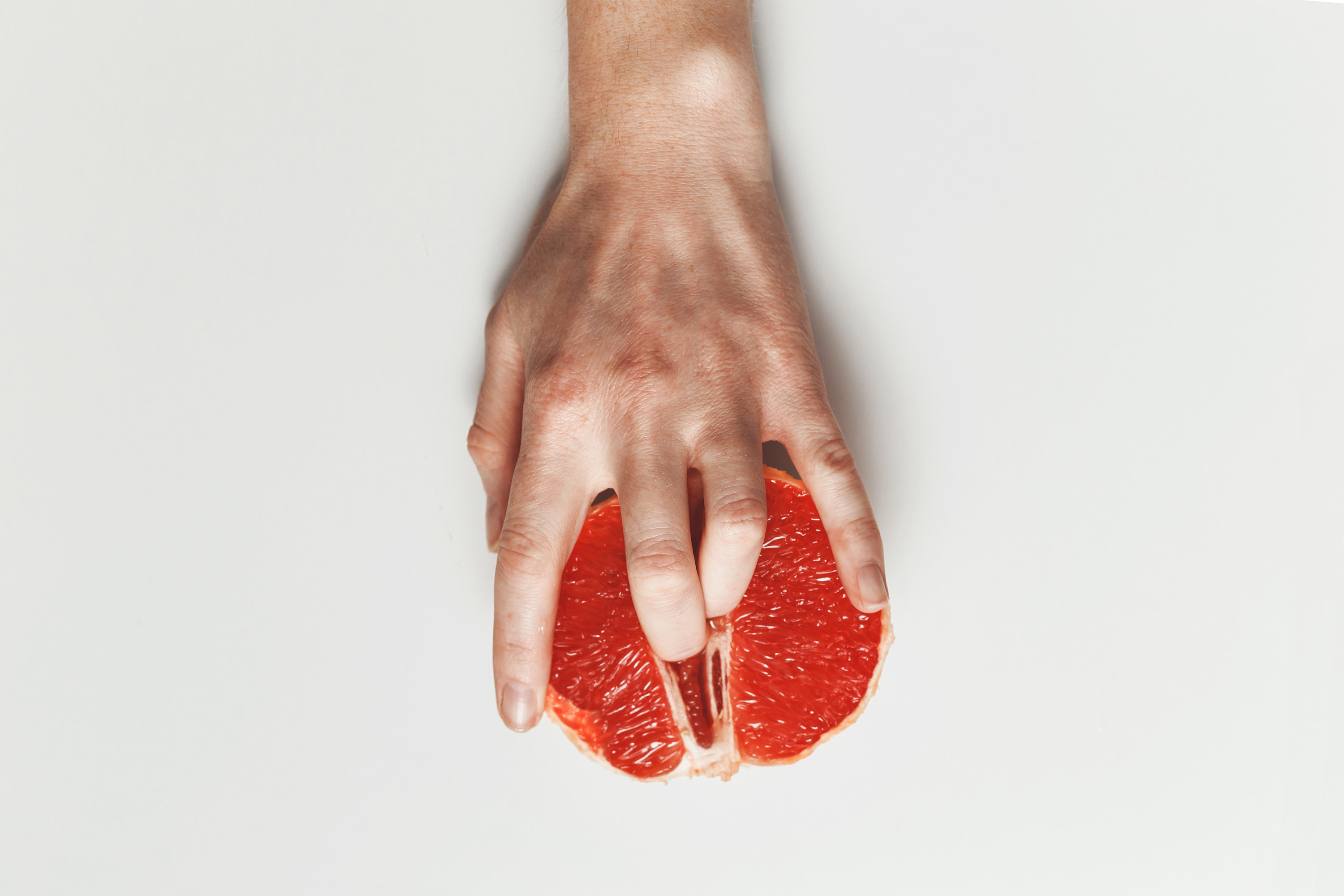 A human hand putting two fingers into a grapefruit on white background
