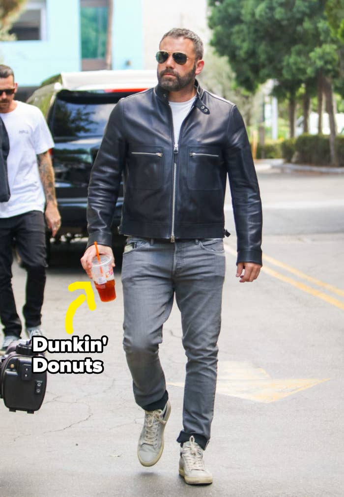 Ben Affleck walking down the street in jeans and a leather jacket and carrying a Dunkin&#x27; beverage