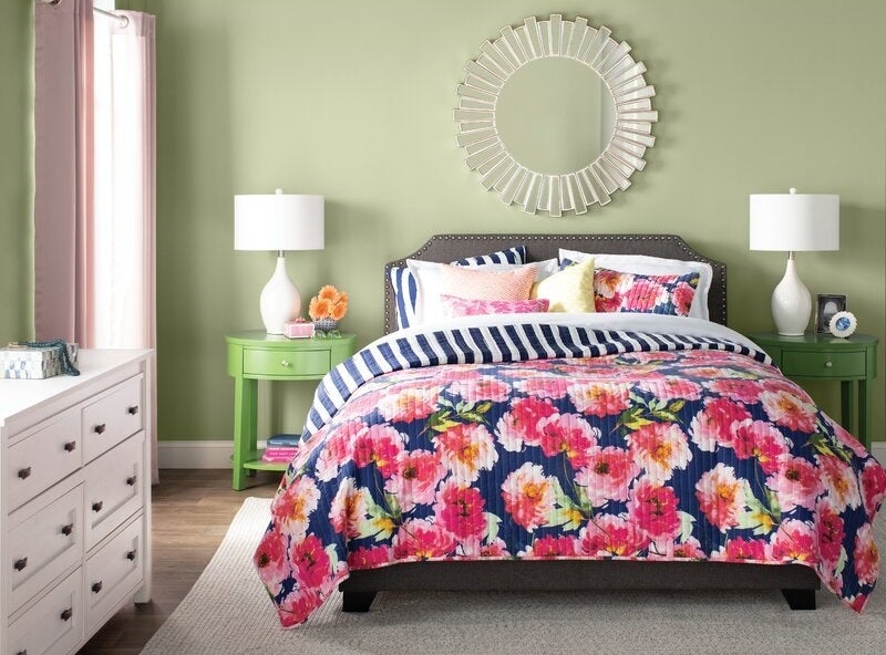 Gray upholstered bed made with colorful floral bedding in a bedroom