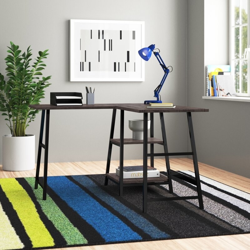 Desk on a striped rug in a room with a floor plant and artwork on the wall