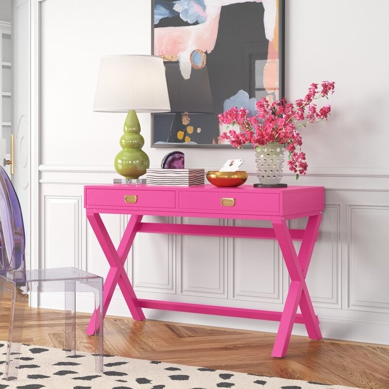 Pink desk styled with bright accessories against a white wall