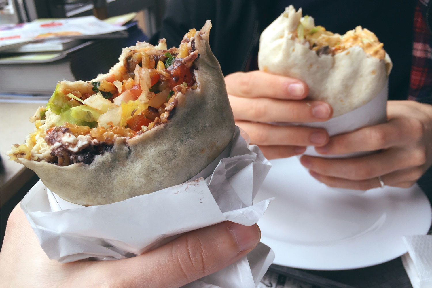 Two people holding burritos.