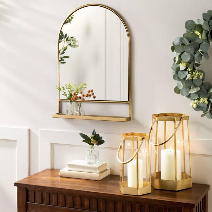 An arched mirror with a gold frame and shelf hung up on a wall