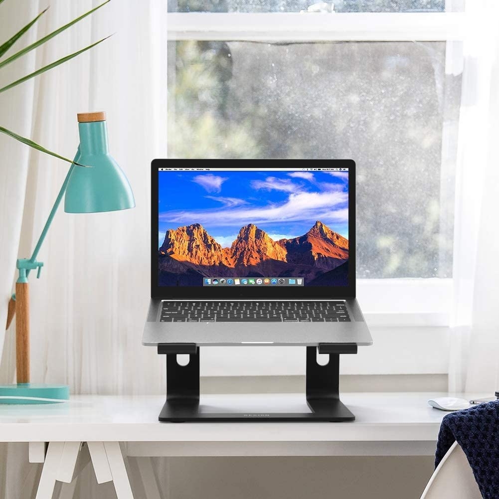A laptop on the stand on a desk with a lamp next to it