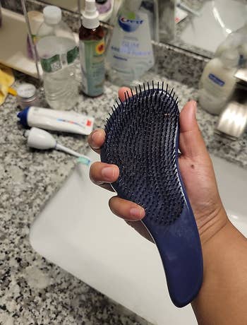 reviewer holding the turquoise detangling brush