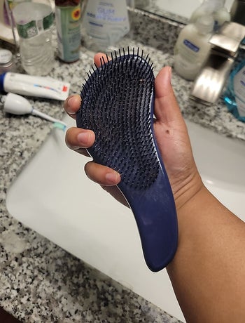 reviewer holding the turquoise detangling brush
