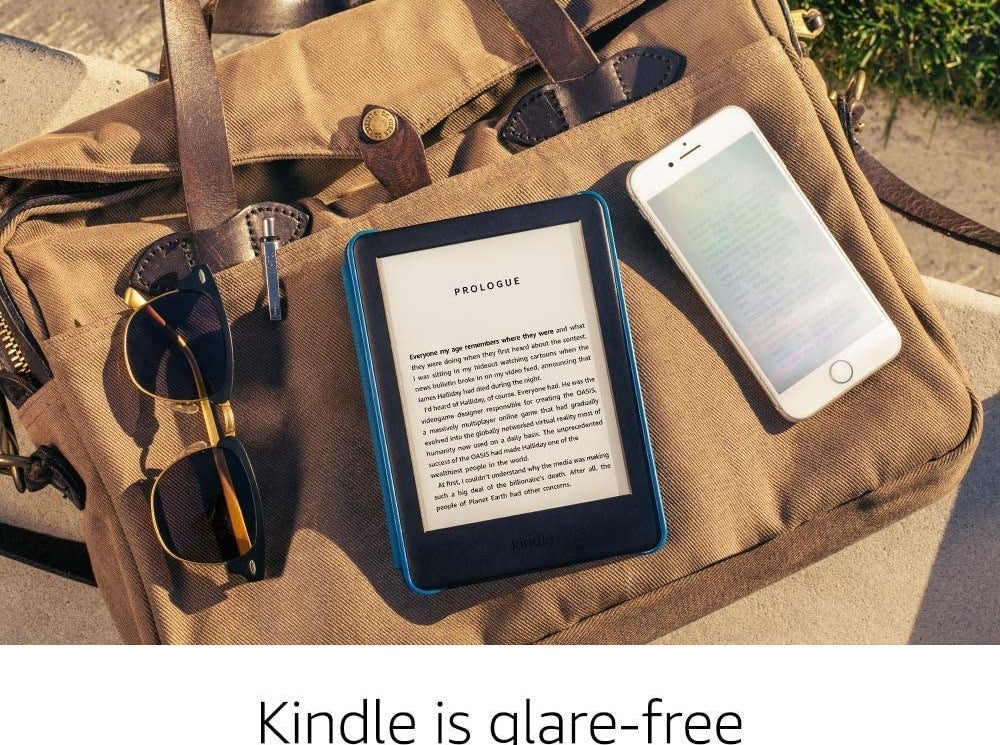 The Kindle on top of a tote bag between sunglasses and a phone