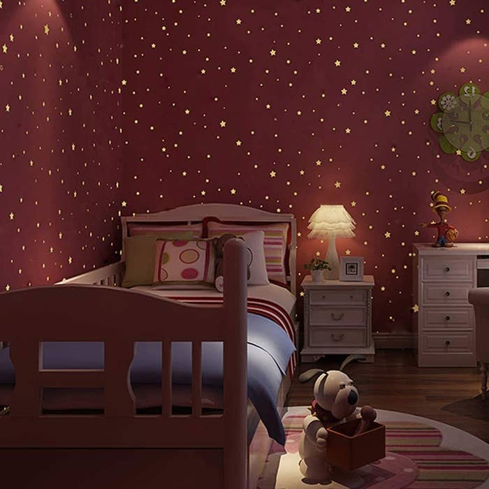 A child&#x27;s bedroom with the glow in the dark stickers all over the walls, with a bed, table, and toys around the room
