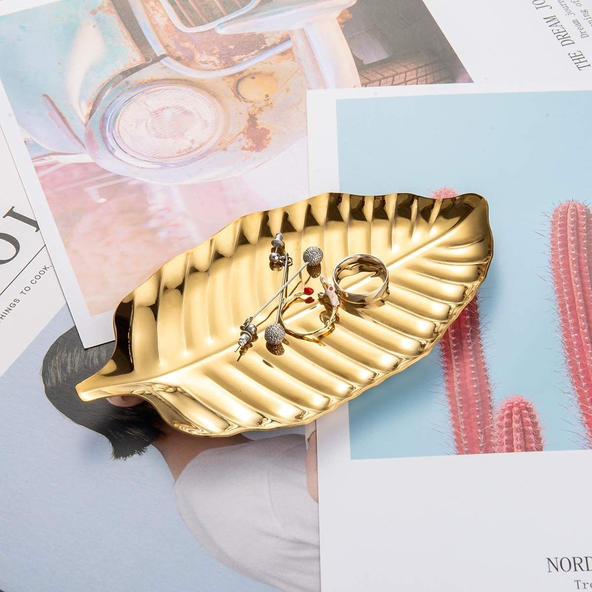 The gold leaf tray holding some earrings and rings on a stack of magazine pages