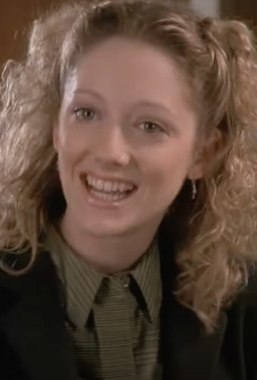 Greer with curly hair, buttoned-up shirt, and blazer