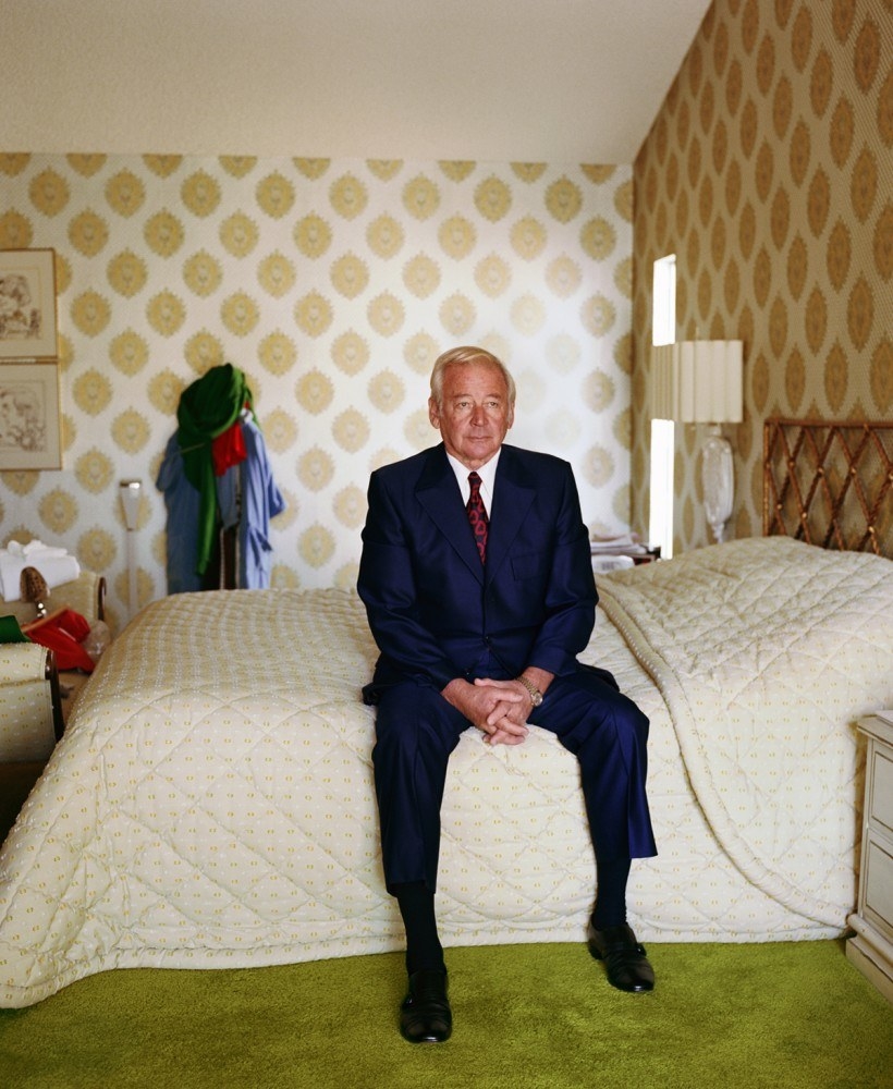 a man in a suit sitting on a bed at home