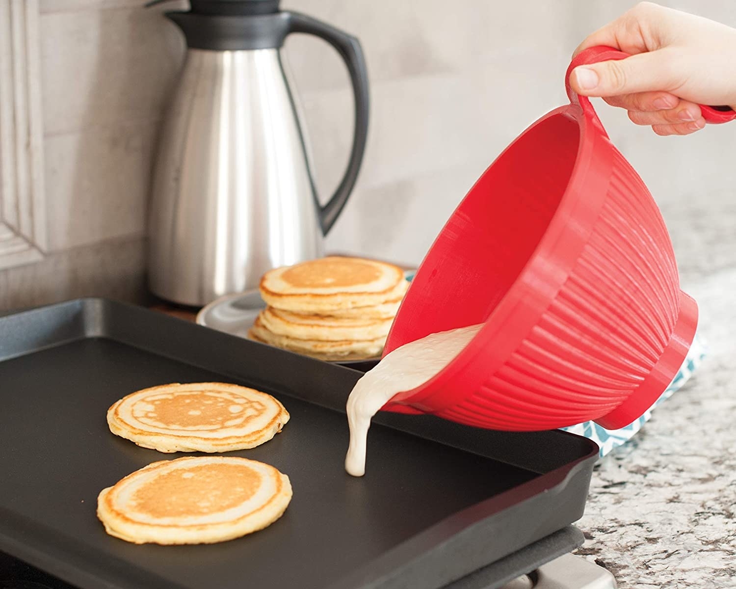 A person poring pancake batter from the bowl onto a griddle