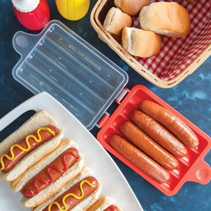 Four hot dogs in the steamer surrounded by cooked weenies and buns