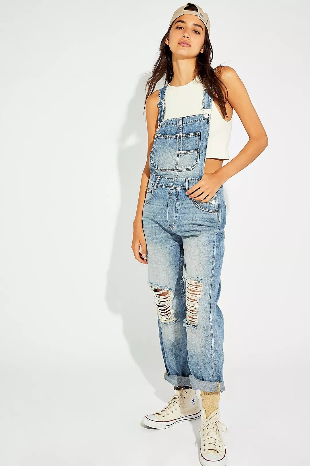 model wearing denim overalls with distressed holes in the middle of the knee are