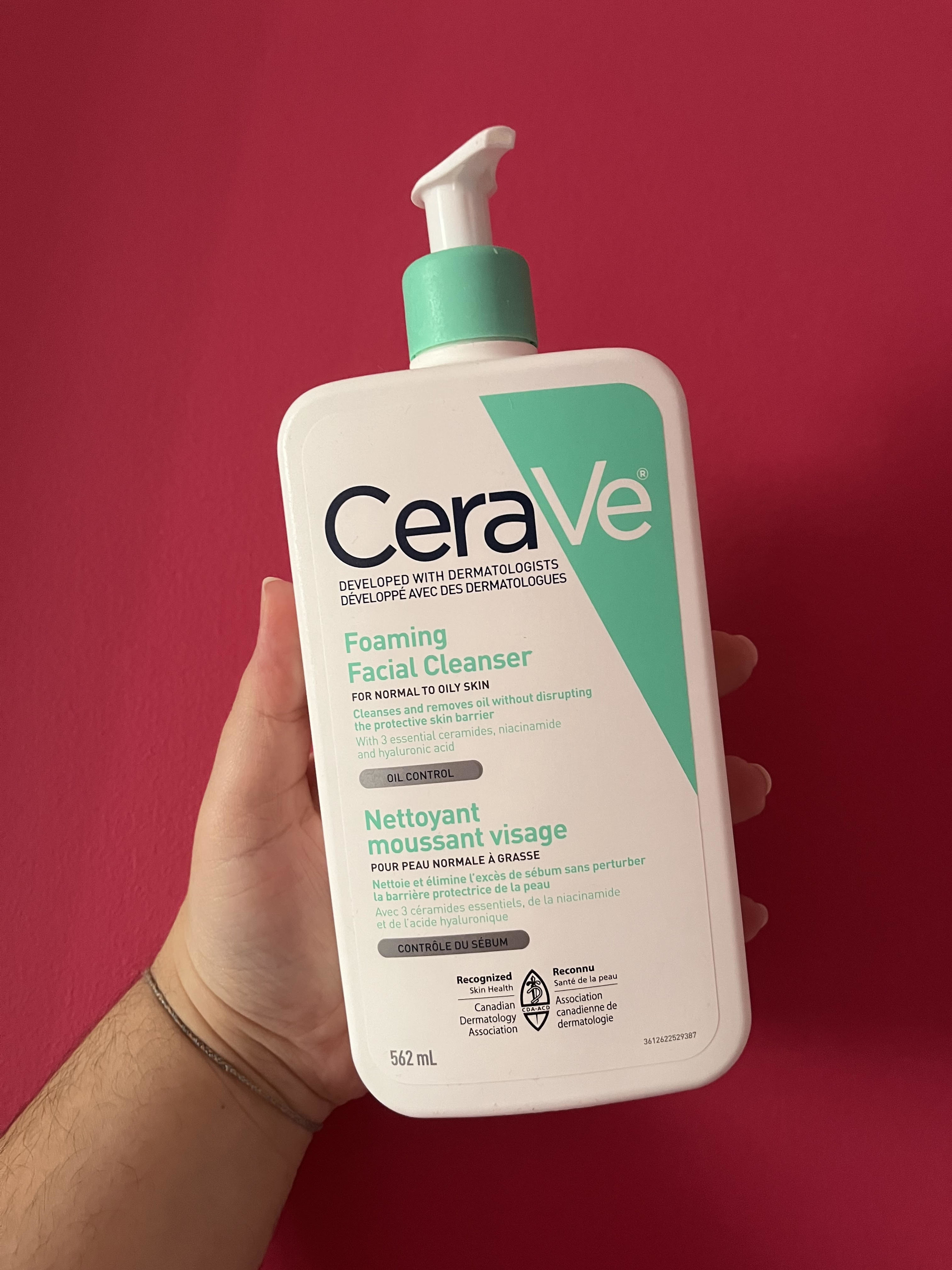 Bianca&#x27;s hand holding up a bottle of the CeraVe cleanser against a plain wall