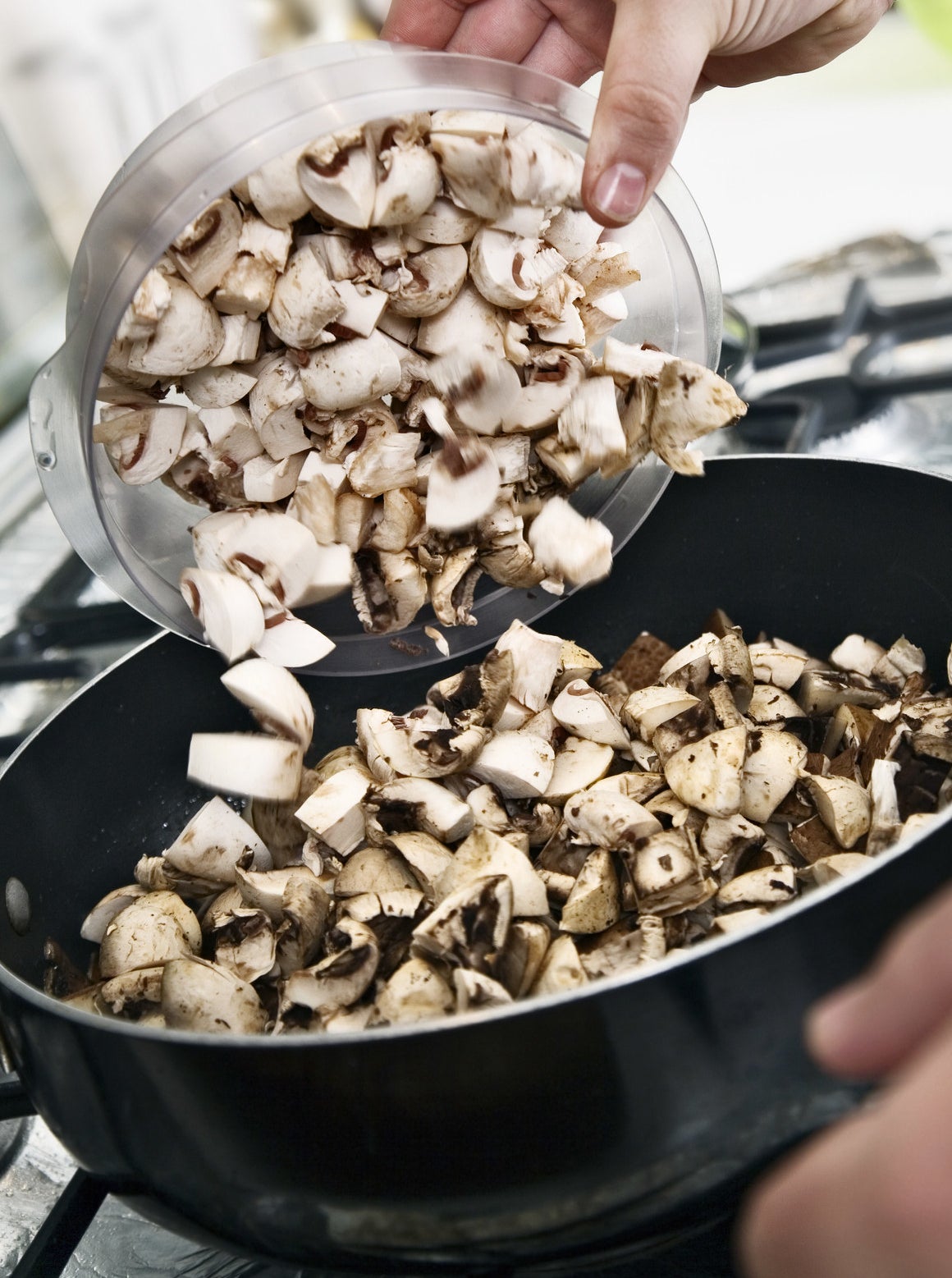 A cook pouring sliced mushrooms into a pan