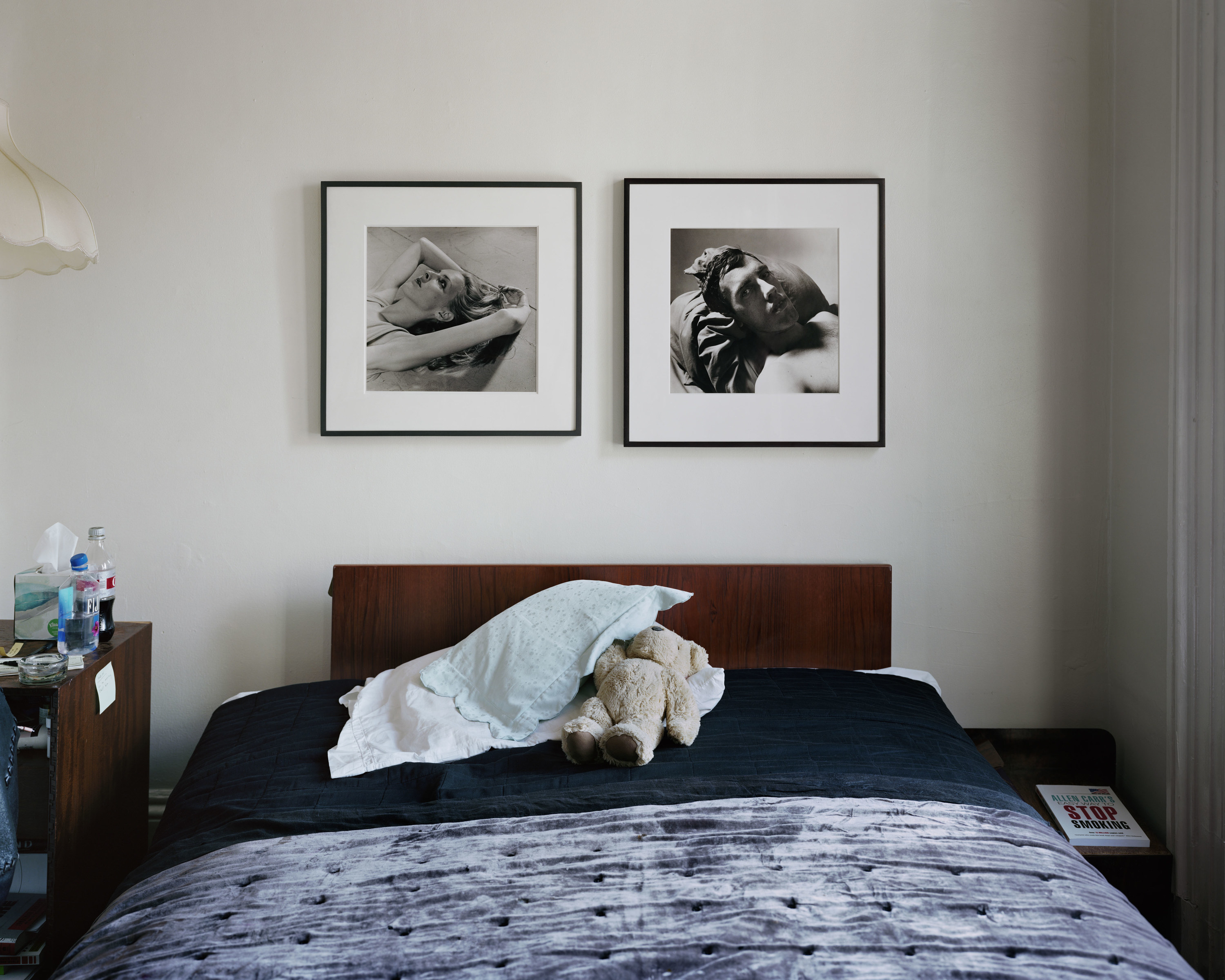 a bed with pillows and teddy bears and two framed photos of a man and a woman above it 