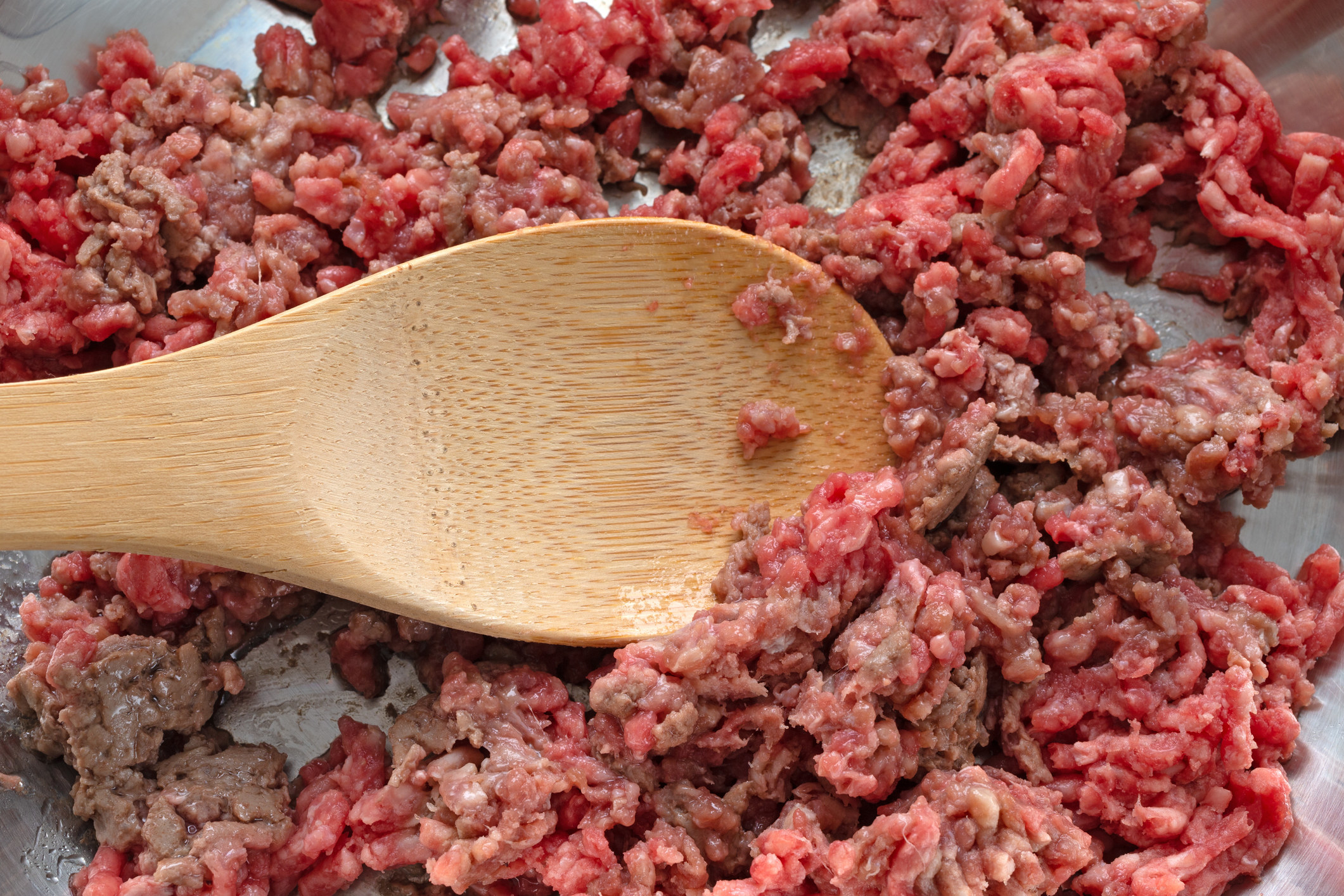 Browning hamburger in a pan with a wood spoon