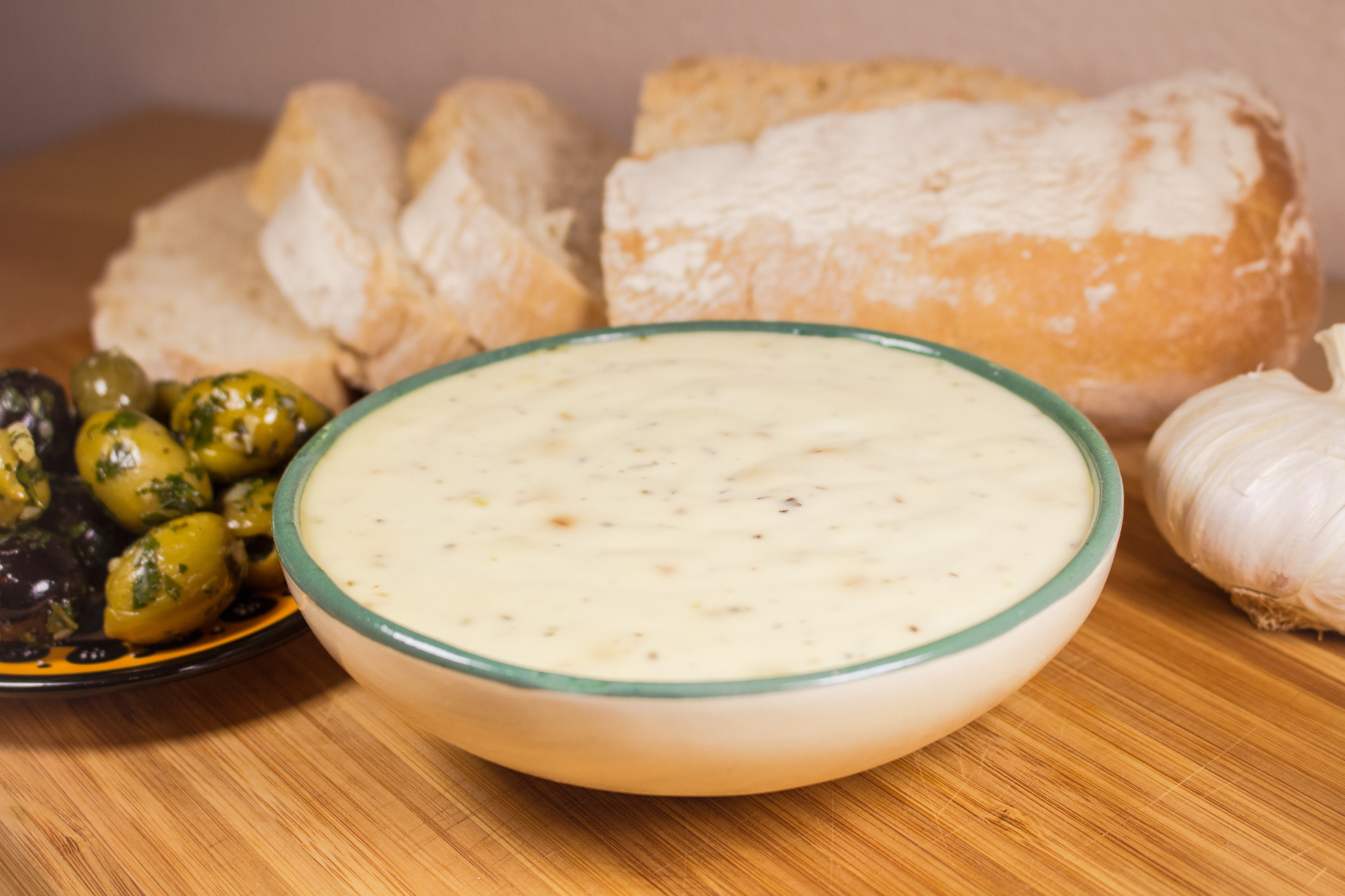 Homemade aioli in a bowl with bread and olives.