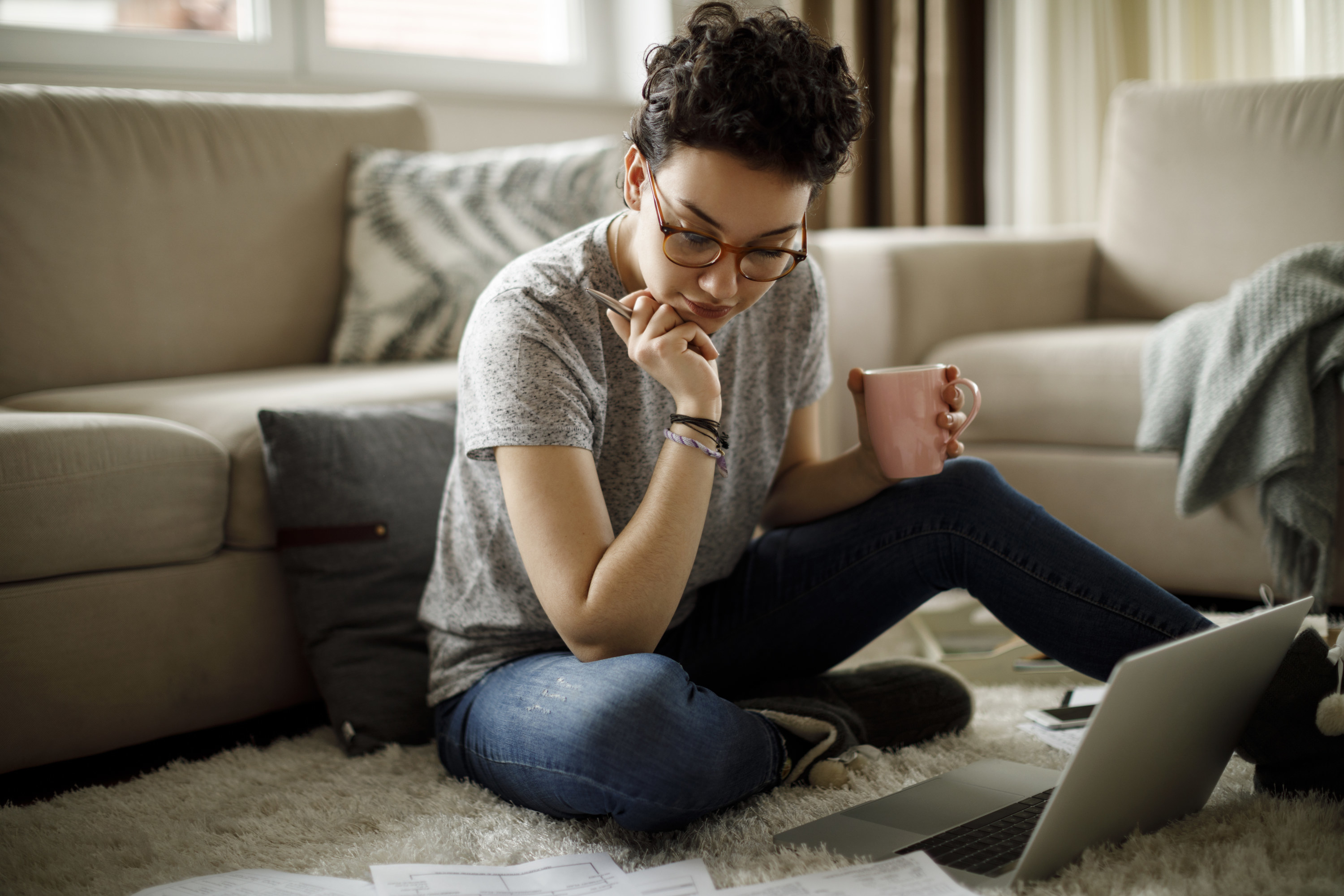 Woman looks a papers on the floor with her laptop open