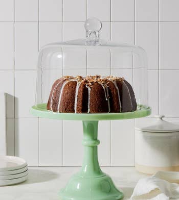 the green cake stand holding a cake that's covered with a glass dome