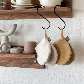 two kitchen gloves hanging on a hook from a kitchen shelf
