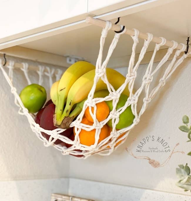 the white product basket attached to the bottom of a cabinet and holding fruit