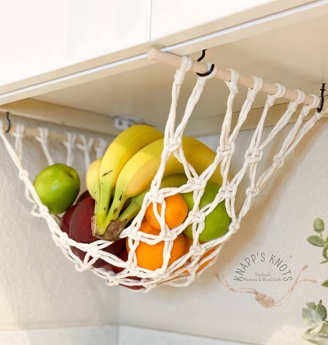 the white product basket attached to the bottom of a cabinet and holding fruit