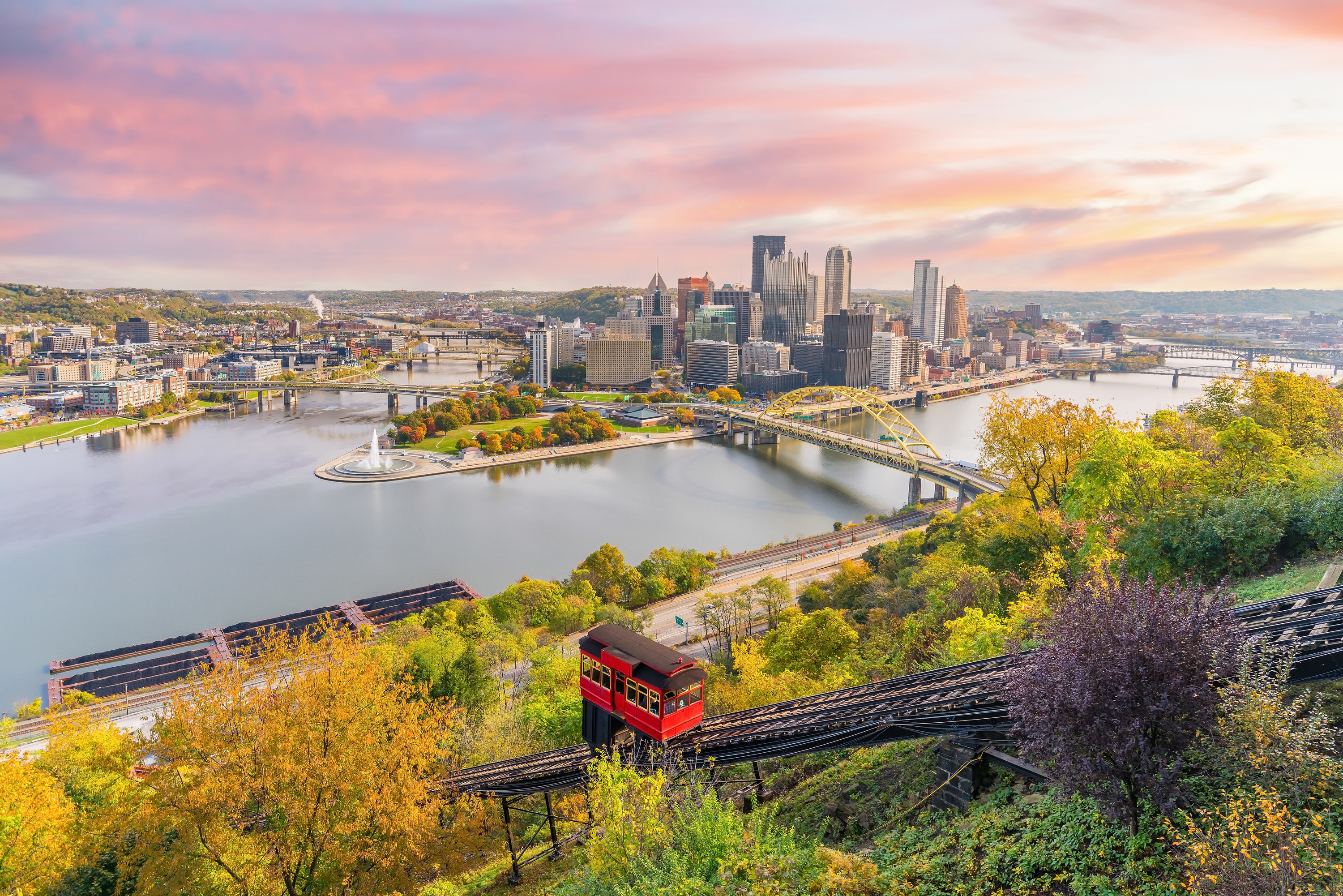 Landscape shot of Pittsburgh skyline at sunset with a red incline car climbing up the track in the foreground