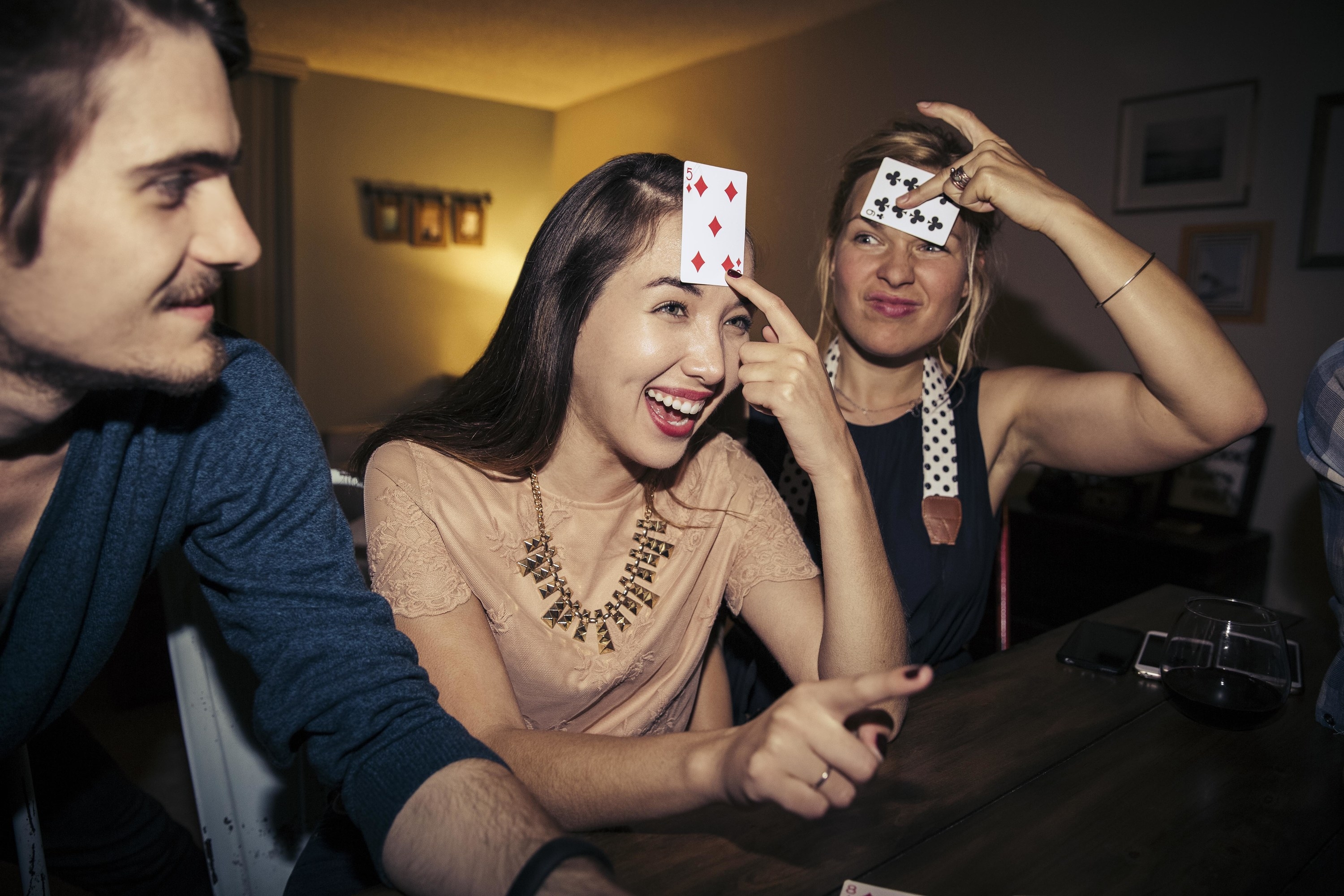 A man sitting next to two women who are holing up cards to their foreheads