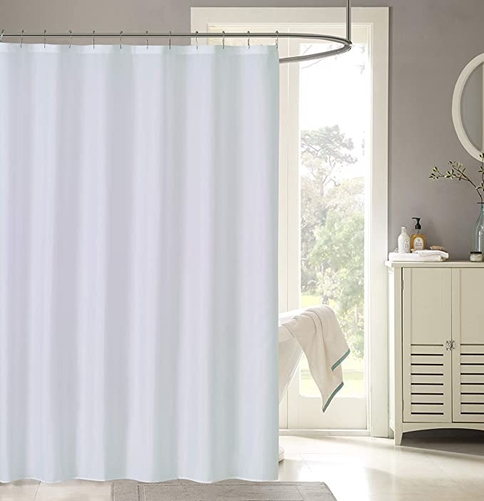 A plain shower curtain liner hanging over a bath in a bathroom