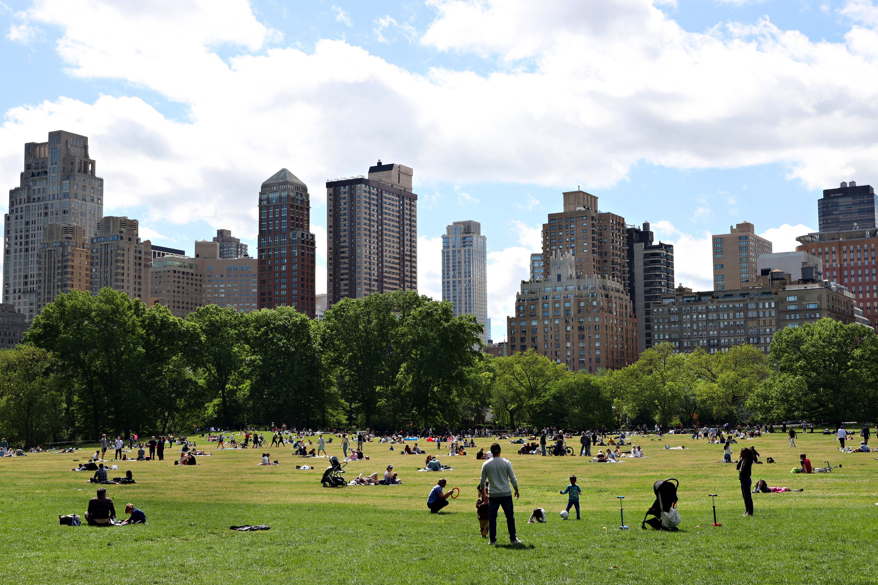 Lots of people in Central Park, New York playing games and relaxing while looking at the Midtown skyline