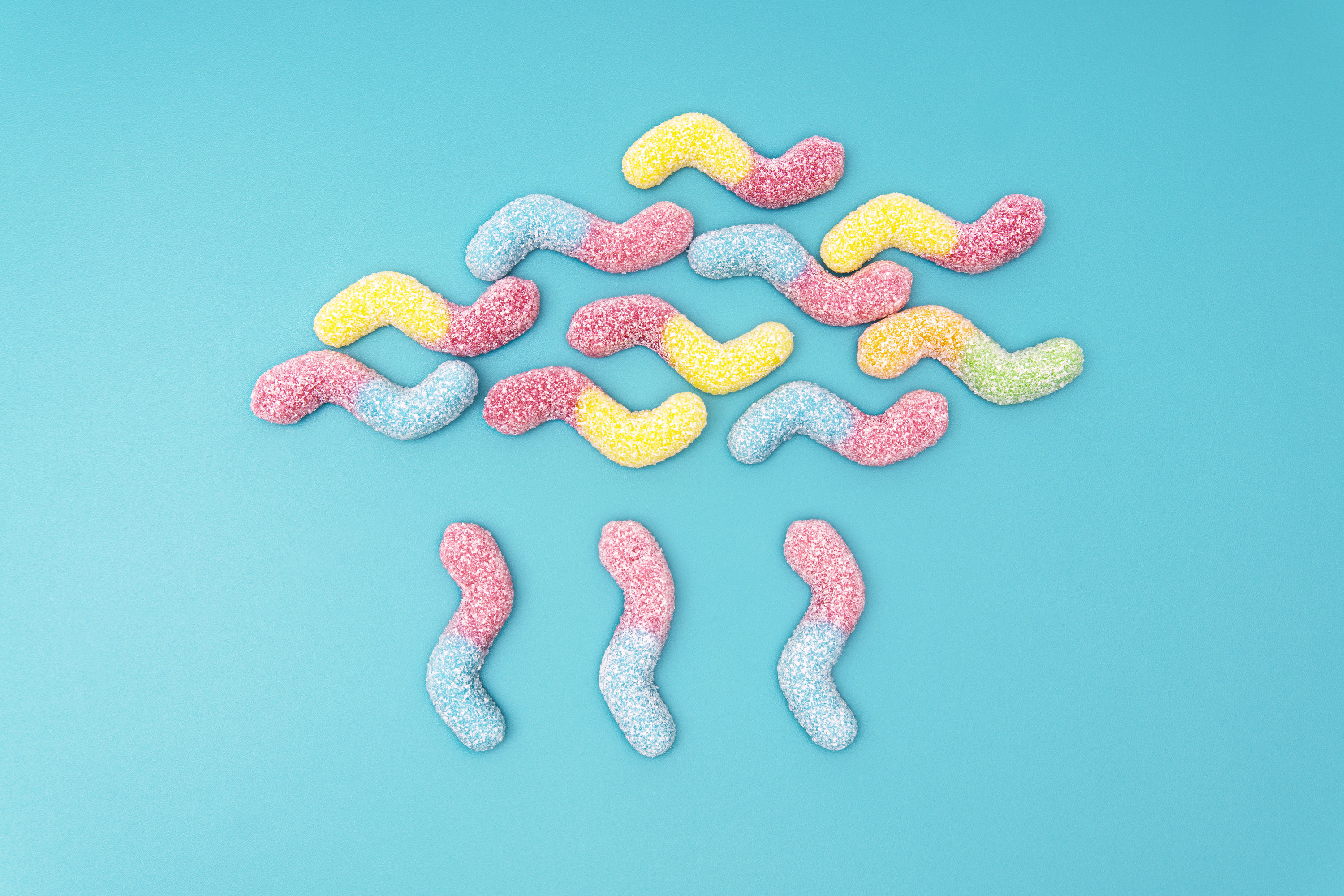 Creative raining cloud flat lay made of colored sugar coated gummy worms on a light blue background