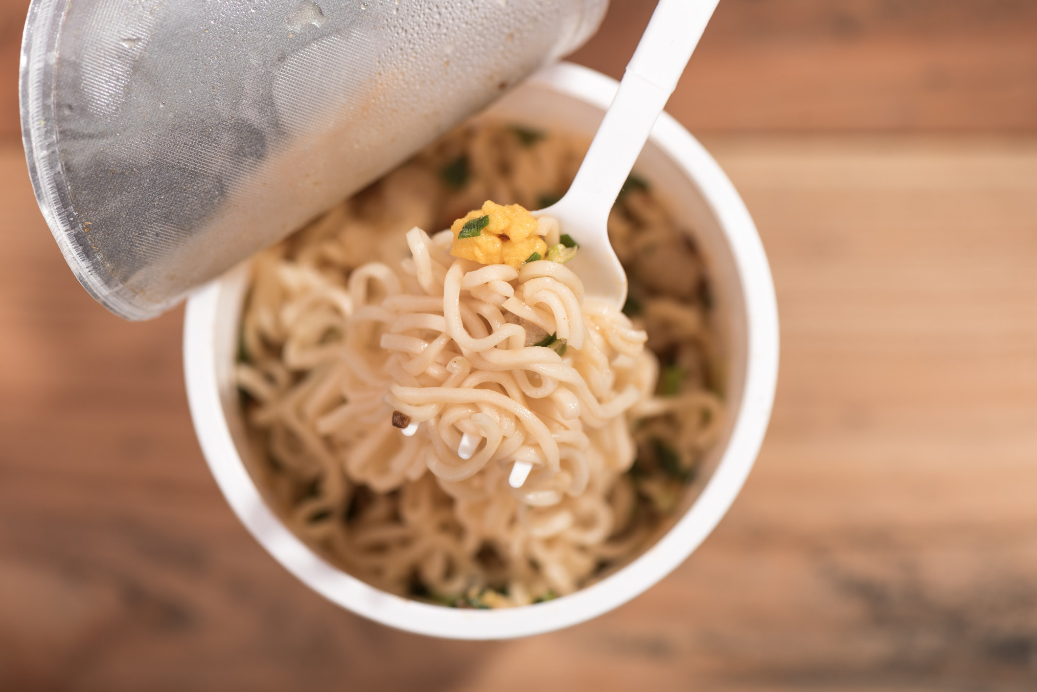 A stock image of an overhead view of ramen noodles in a cup with some noodles on a fork