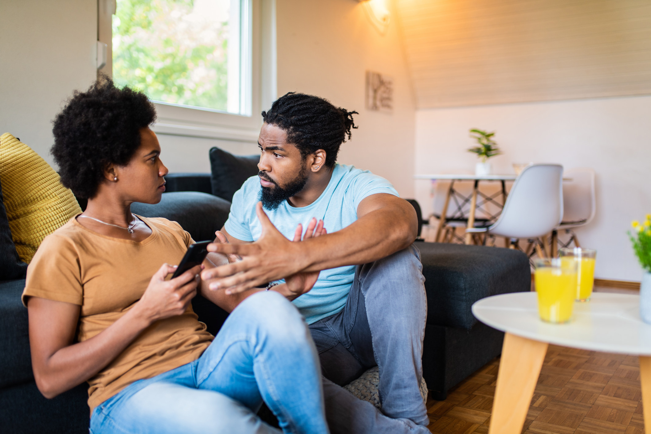 Couple arguing on the floor in front of the couch as the wife holds her phone