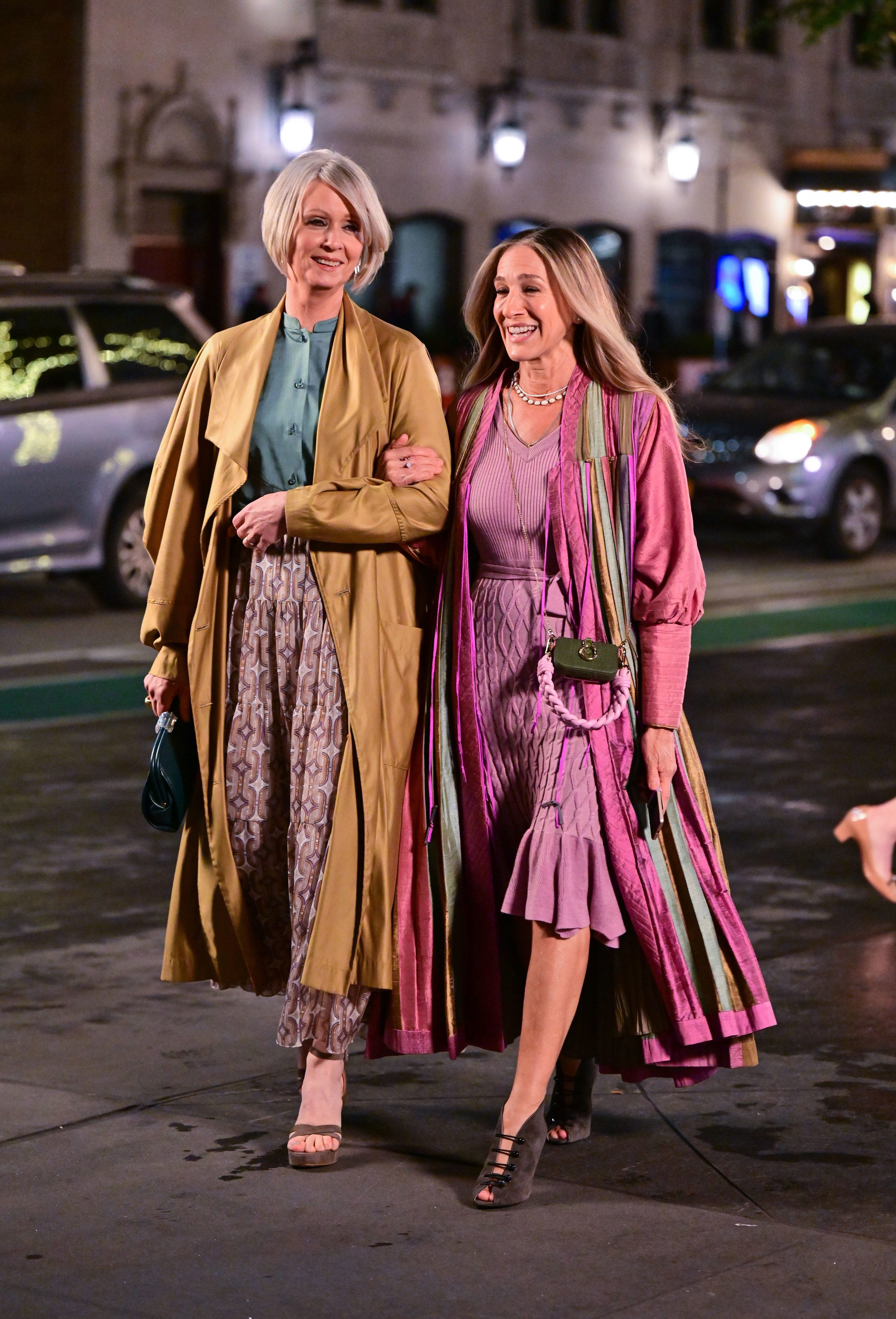 Miranda and Carrie walking down the street at night arm-in-arm