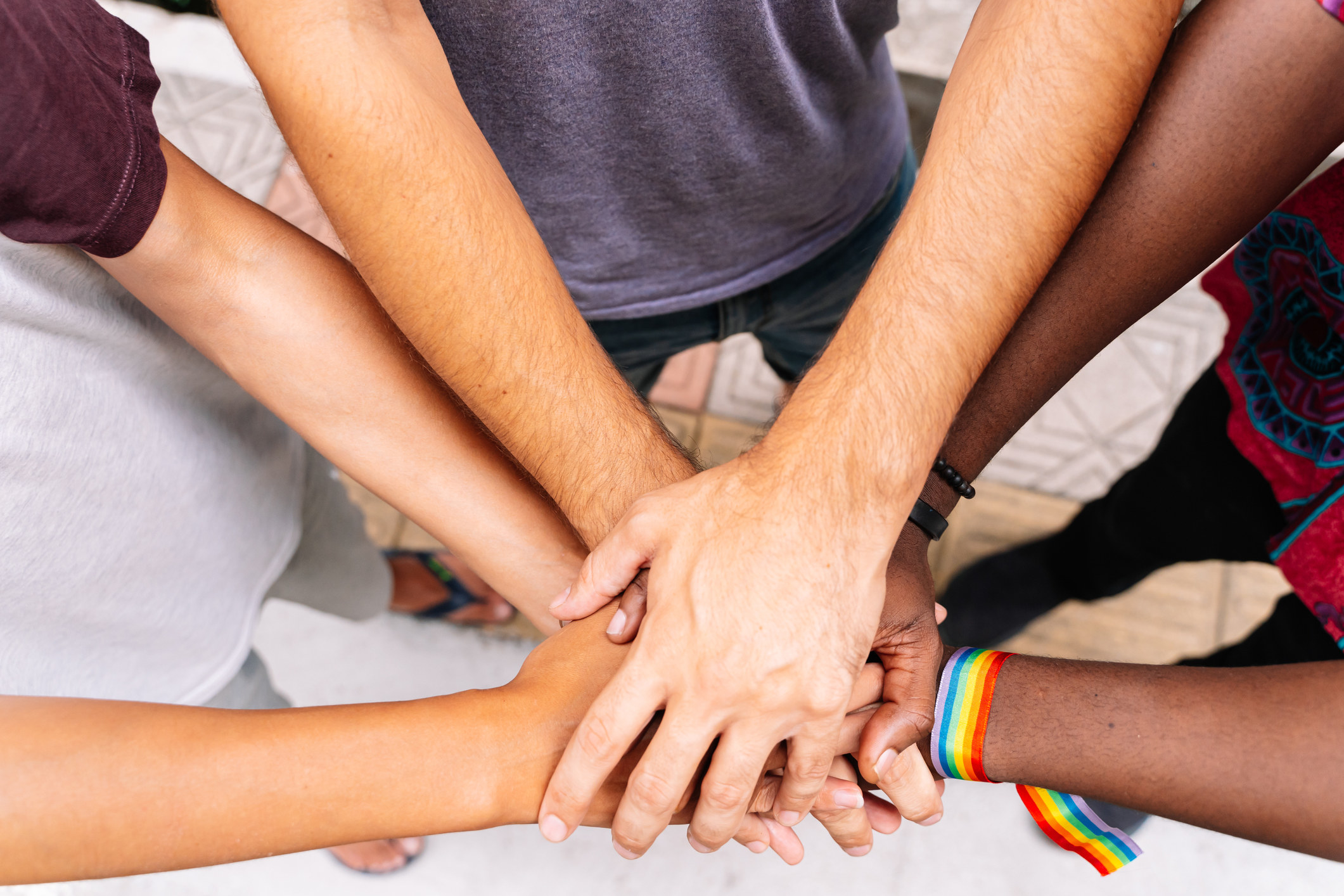 Hands of a group of people of different ethnicities with an LGBT flag bracelet