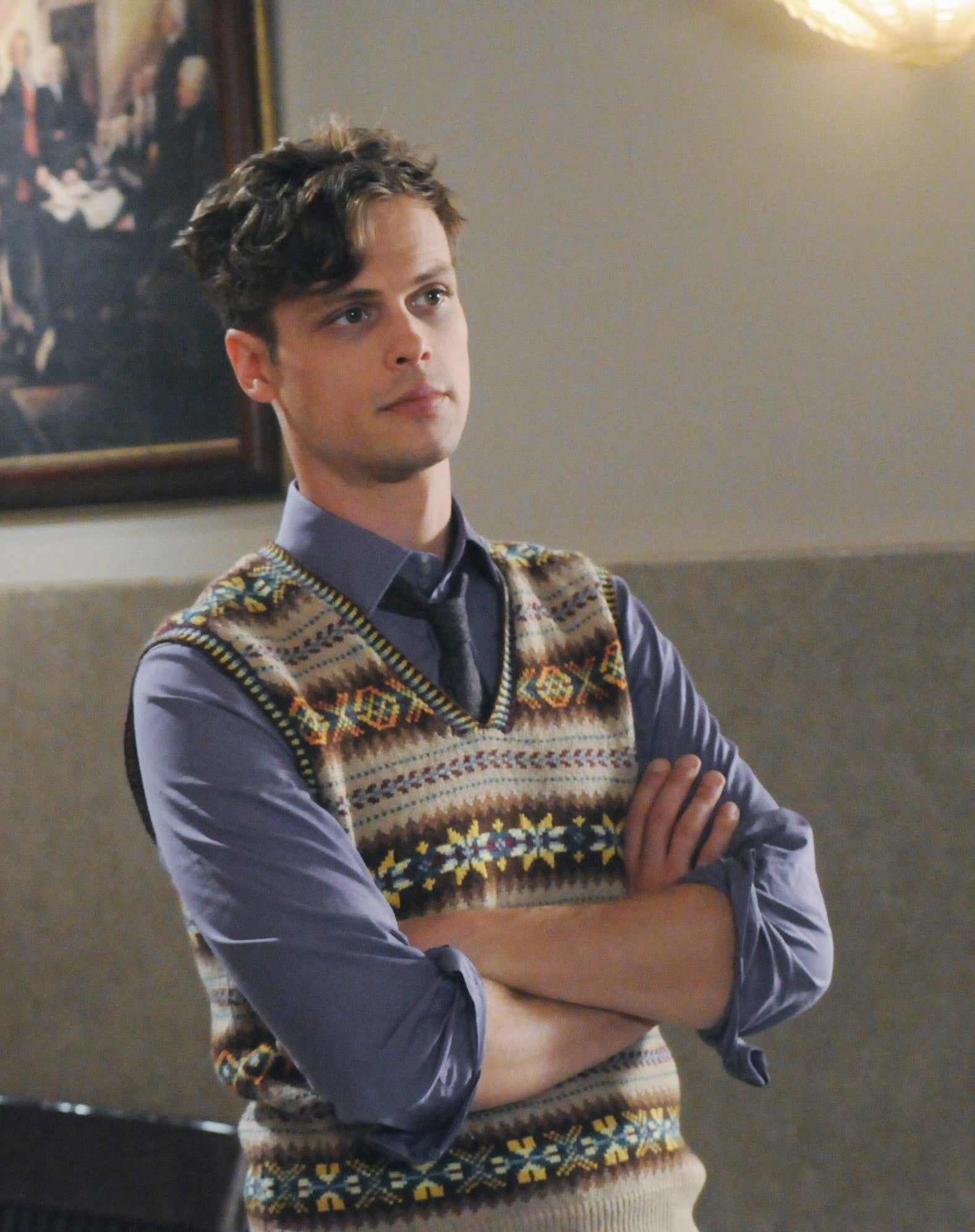 Reid wearing a sweater vest with his arms crossed
