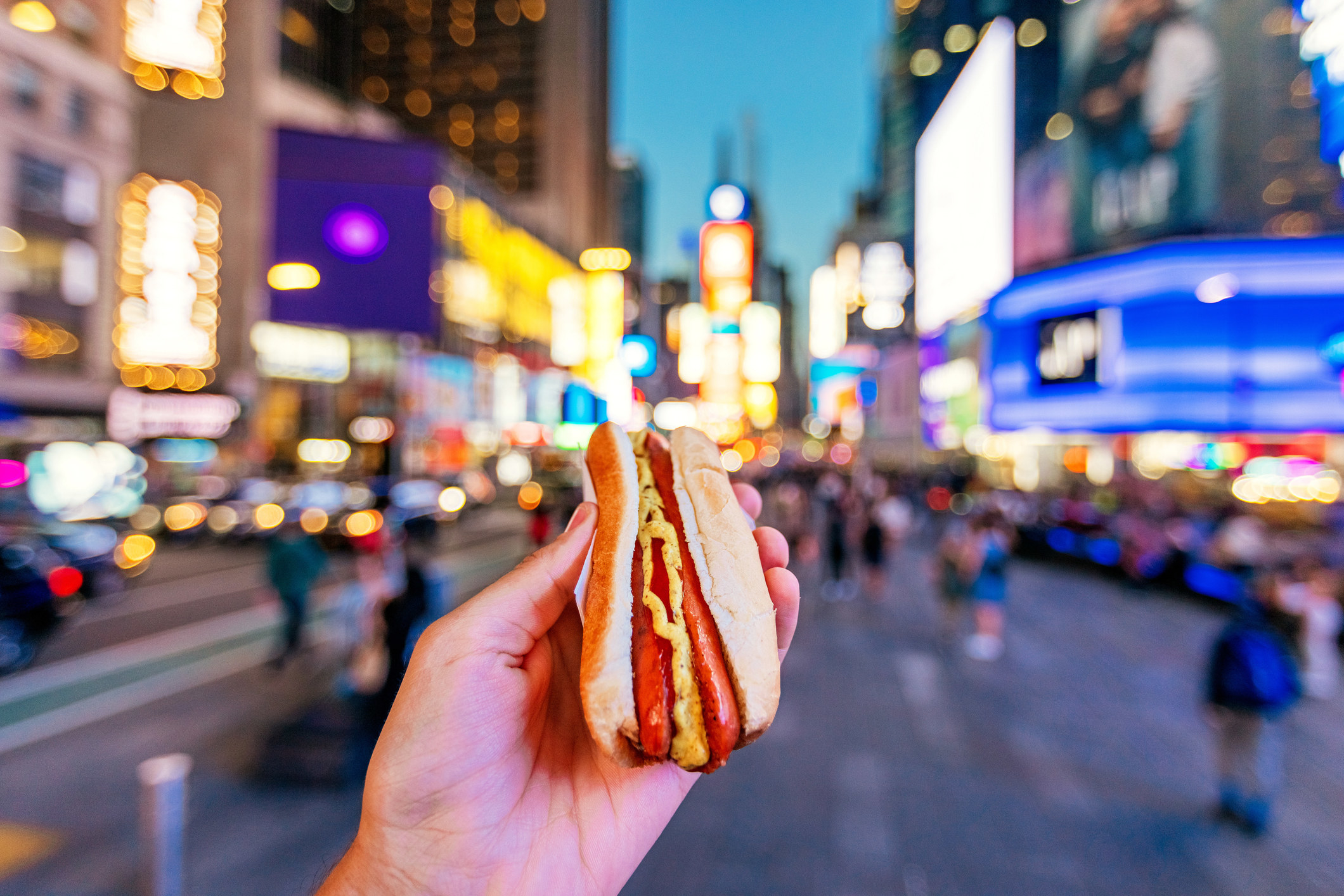 A man holding a street hot dog in NYC.