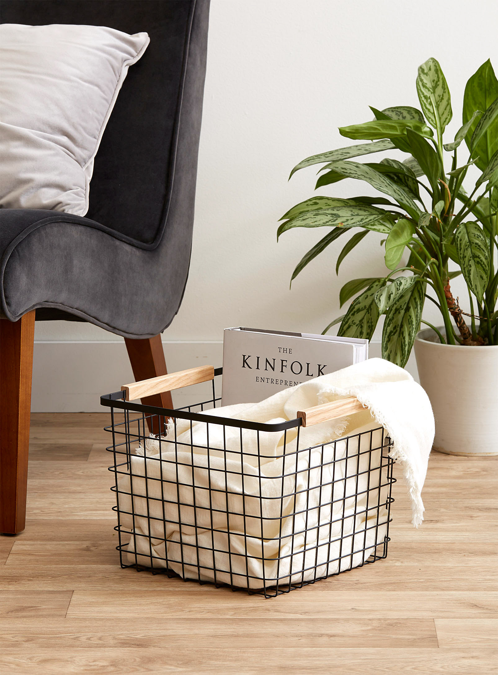 A wire basket on a wooden floor with a large book and a blanket inside