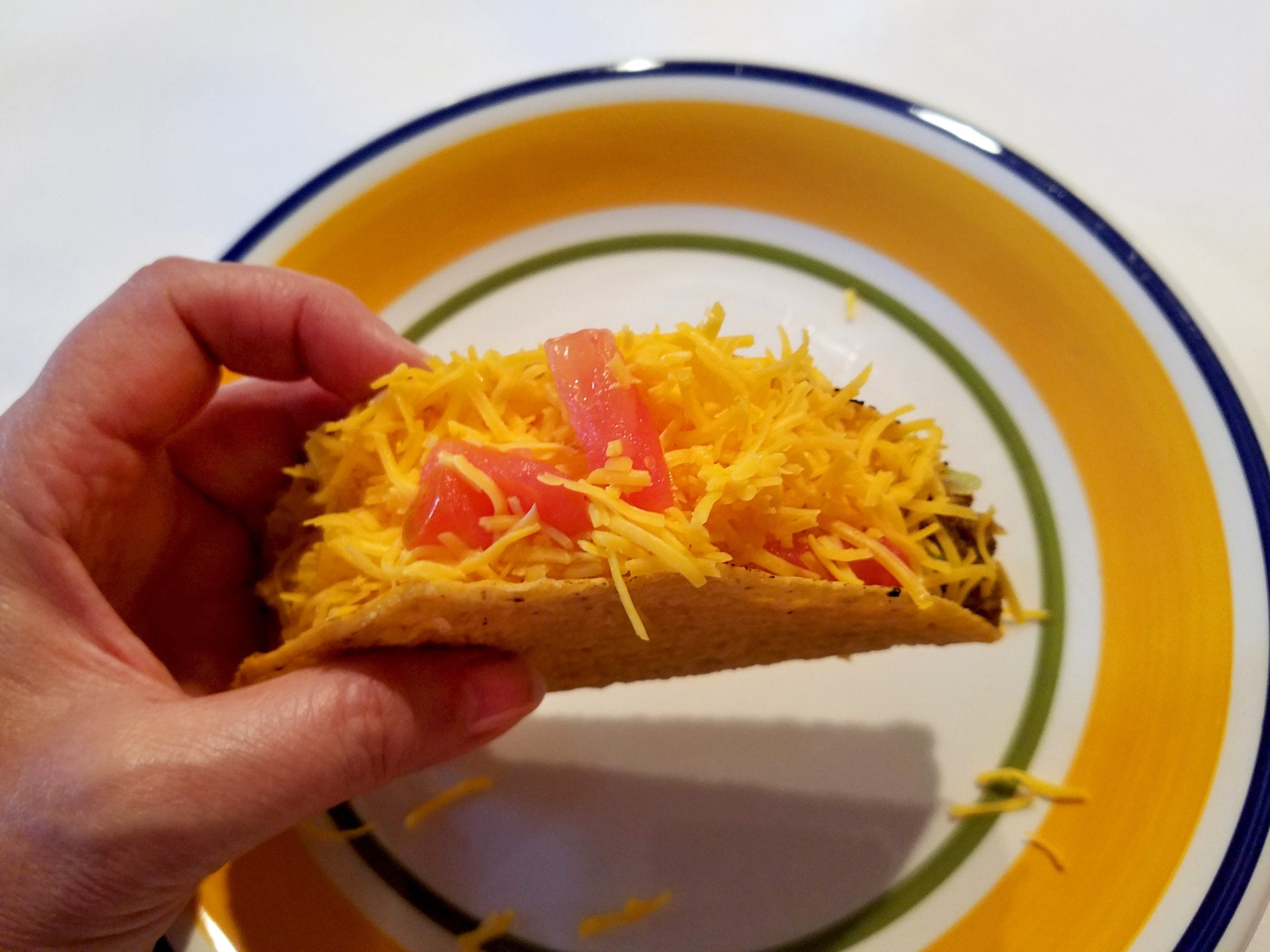 A hand holding a hard taco with lots of cheese.