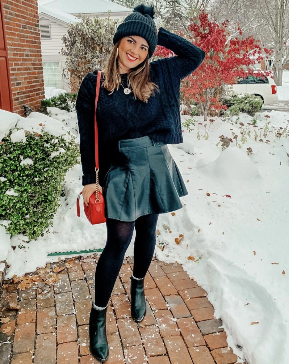 reviewer in short faux leather skirt, tights, and sweater outside in snow
