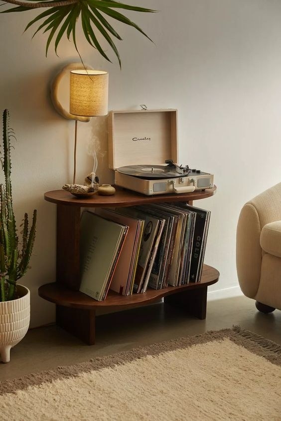 The vinyl storage rack holding records underneath with a turntable on the top shelf next to a lamp