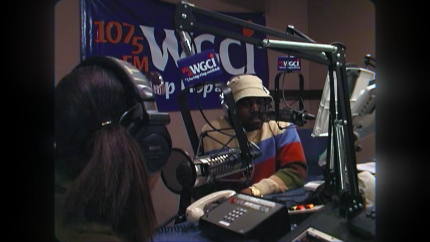 Kanye doing a radio interview while wearing a bucket hat and striped long-sleeved shirt