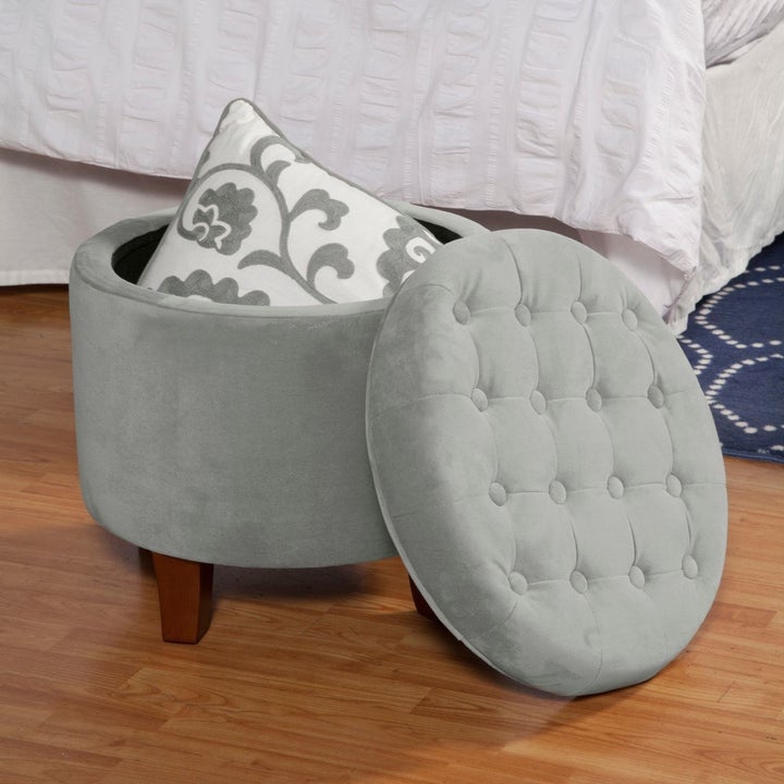 A grey velvet storage ottoman on a floor