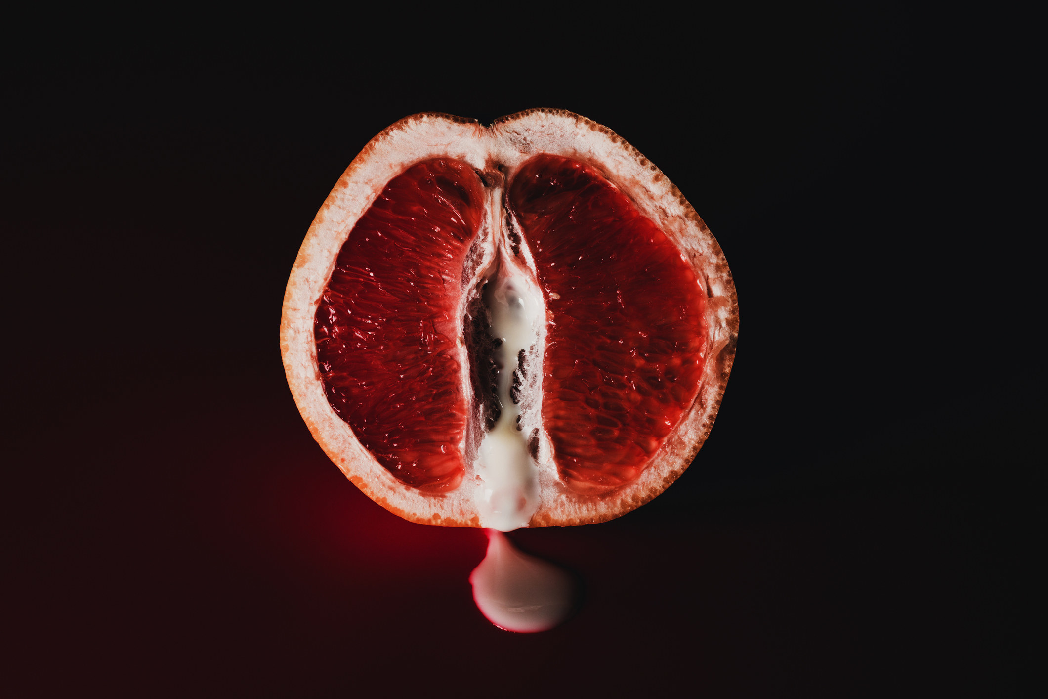Stock image of a fruit with a red-like substance dripping out in front of a black background