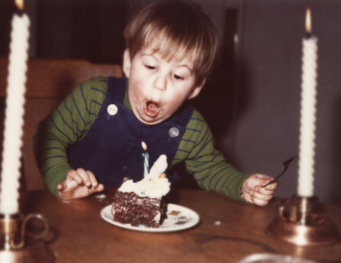 A cute little one year old boy blows out the candle on his very first birthday cake