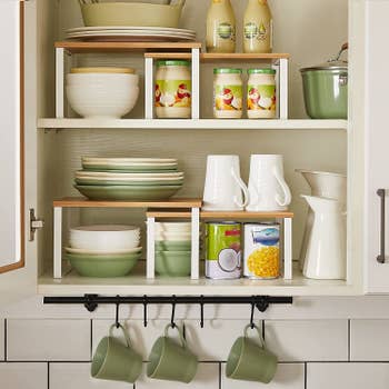 the white organizers in a cabinet holding plates, bowls, and mugs.